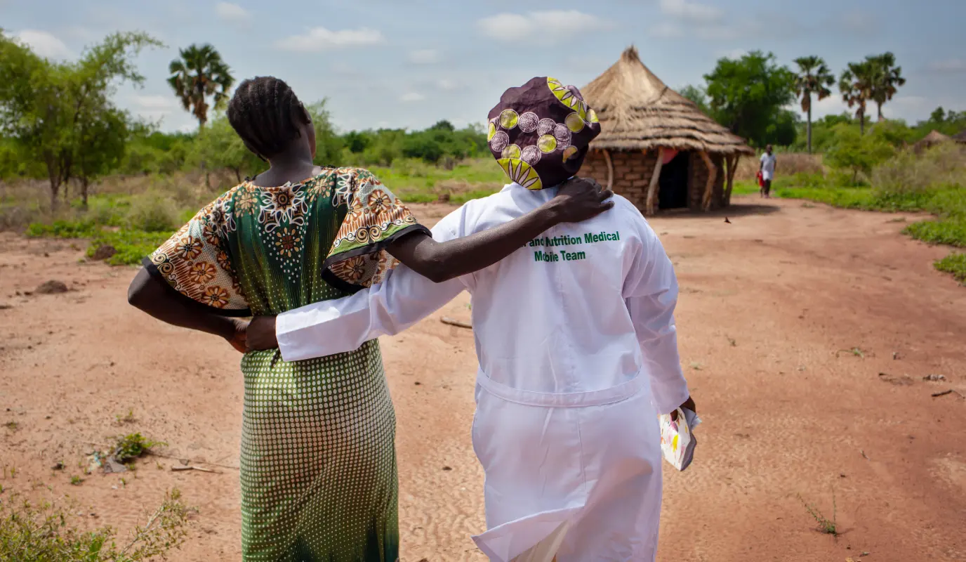 Woman walks with Concern midwife Rebekka at a Mobile Health Clinic in a remote rural area of Aweil, South Sudan.
