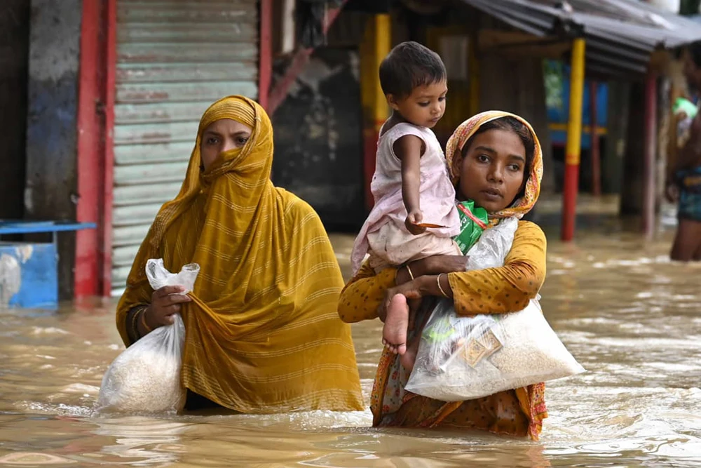 A woman carries a child through flood waters in Bangladesh