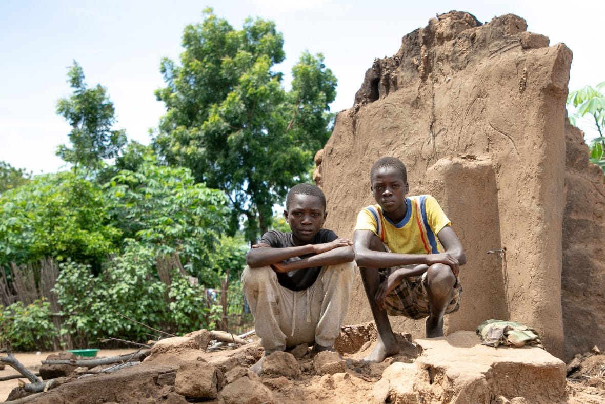 Two boys standing in front of the ruins of their home in Malawi after floods