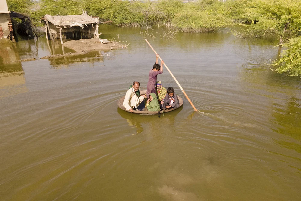 Aqib Aliin (14) transports people on his curry frying pan across the flooded waters in Jhuddo town, Sindh Province during the 2022 floods in Pakistan. (Photo: Emmanuel Guddo/Concern Worldwide)