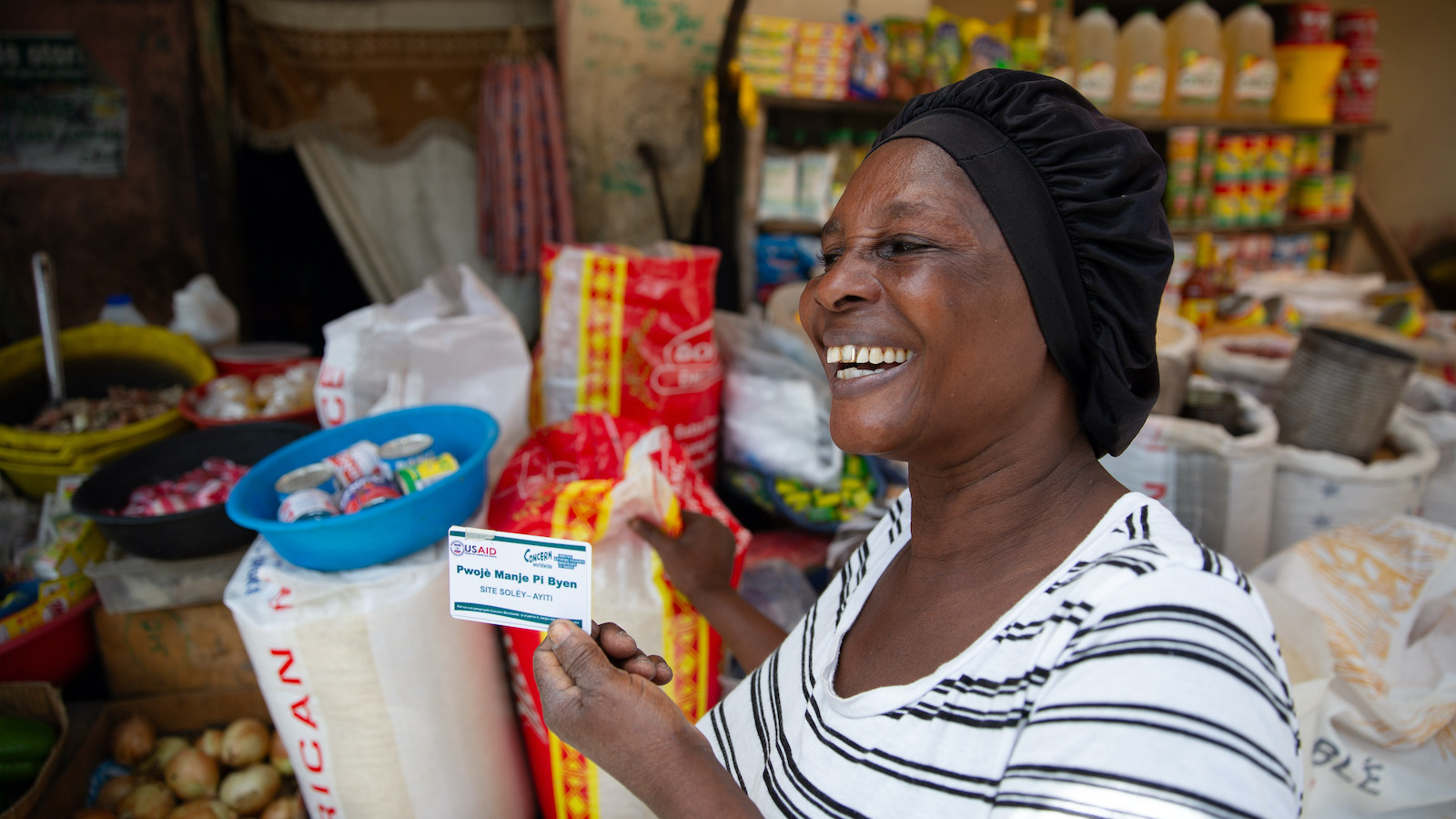 Estelle Adolphe, a participant in the US Government-funded Manje Pi Byen program, uses her account to buy essential provisions from a vendor at a street market in Cité Soleil, Port-au-Prince, Haiti. Photo: Kieran McConville/Concern Worldwide