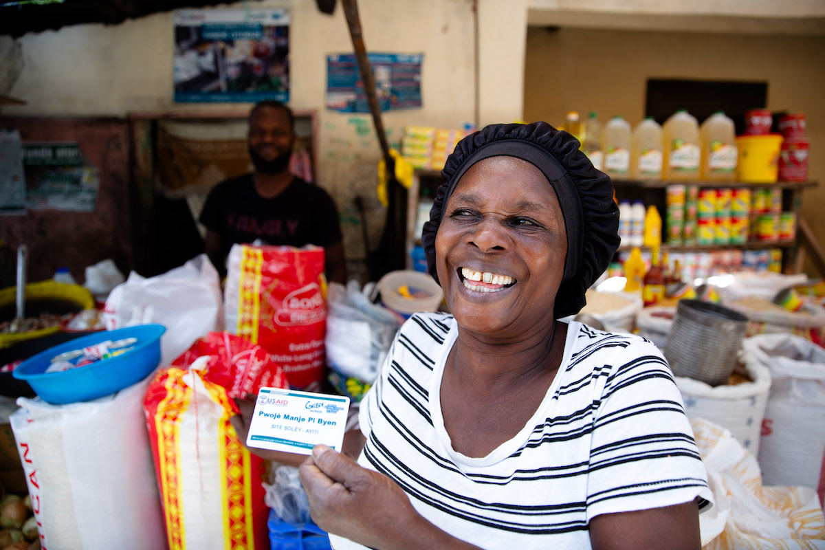 Estelle Adolphe, a participant in the USAID funded Manje Pi Byen program, uses her account to buy essential provisions from a vendor at a street market in Cité Soleil, Port-au-Prince, Haiti. (Photo: Kieran McConville/Concern Worldwide)