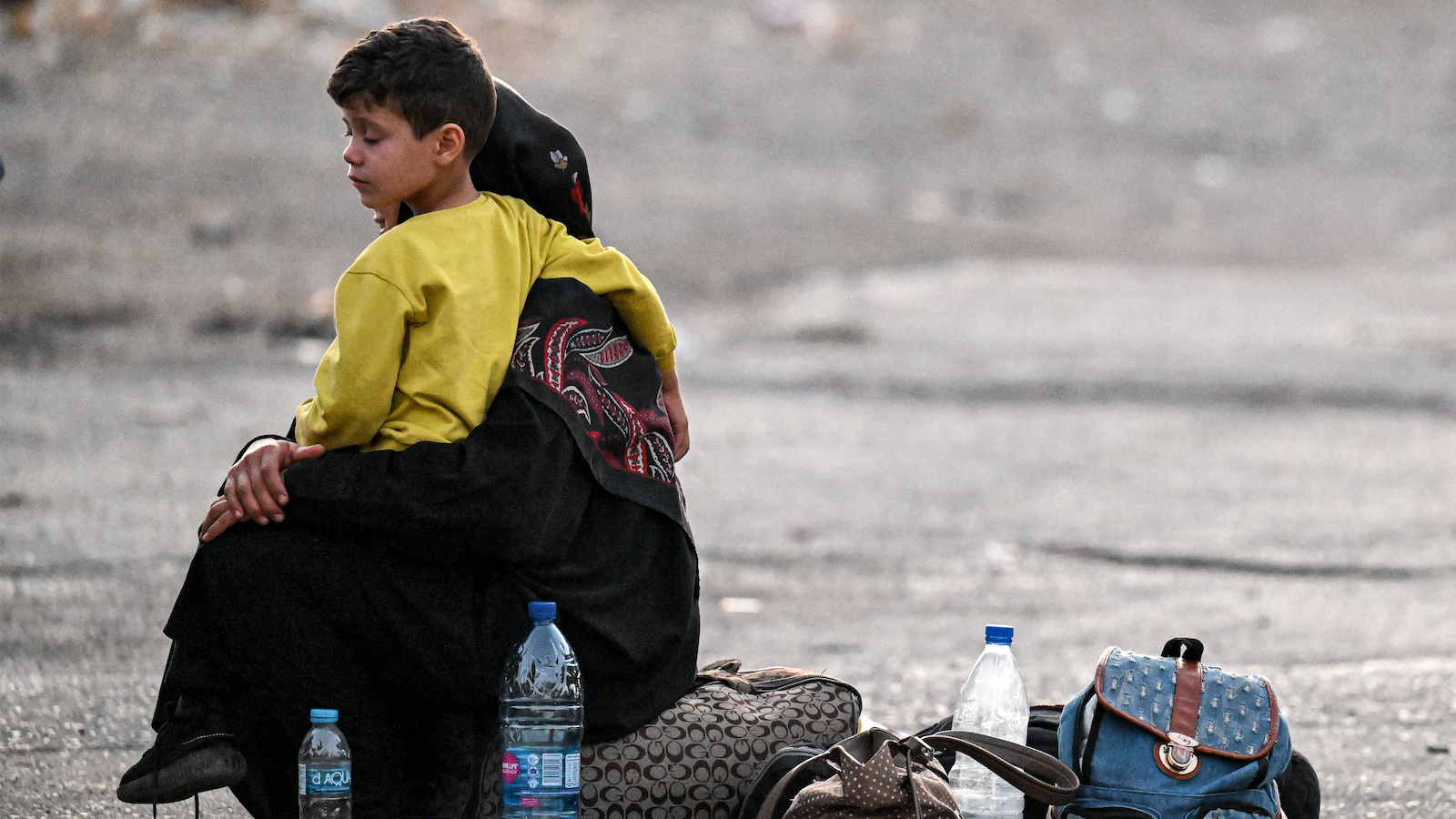 A woman sits with a child on her lap next to bags on the ground as people fleeing from Lebanon arrive on the Syrian side of the border with Lebanon in Jdeidat Yabus in southwestern Syria on September 24, 2024. (Photo: Louai Beshara/AFP via Getty Images)