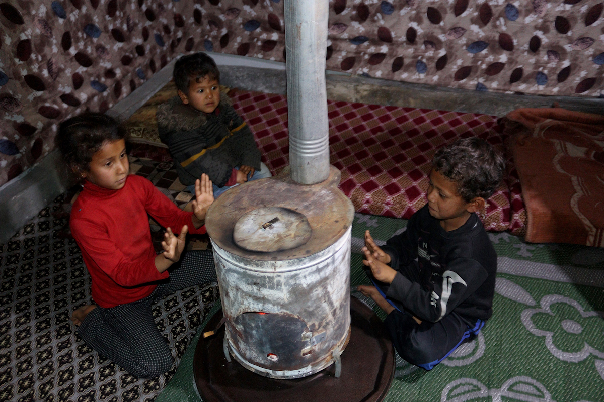 Three of Samira*’s children warm themselves by the stove in their tent. The family of 10 were forced to flee their home in Aleppo early on in the conflict. “We moved from one village to another along the way until we finally ended up here,” says Samira. “We tried not to go too far from our homes, hoping we would return soon — but ‘soon’ turned into years.” (Photo: Concern Worldwide)