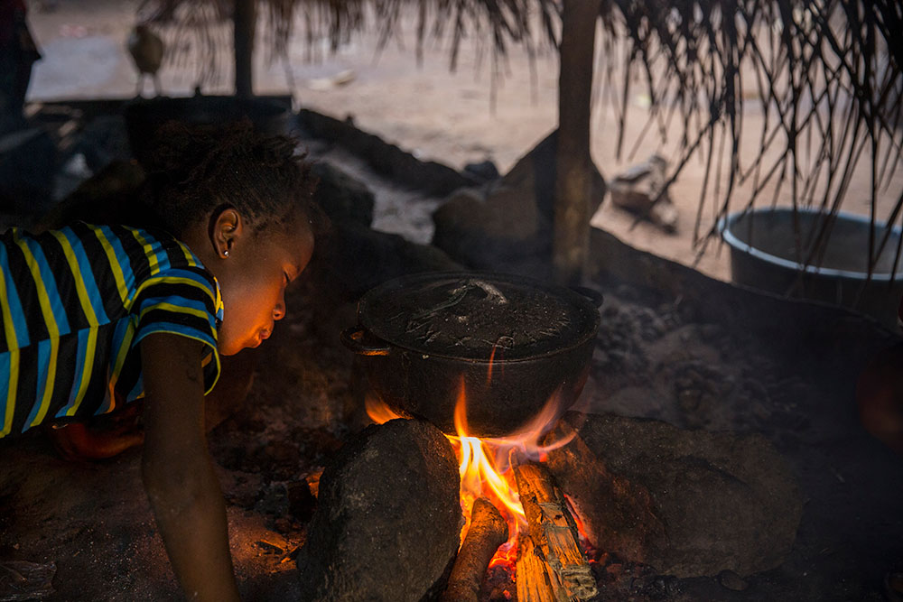 A young girl blowing on a cooking fire in Sierra Leone