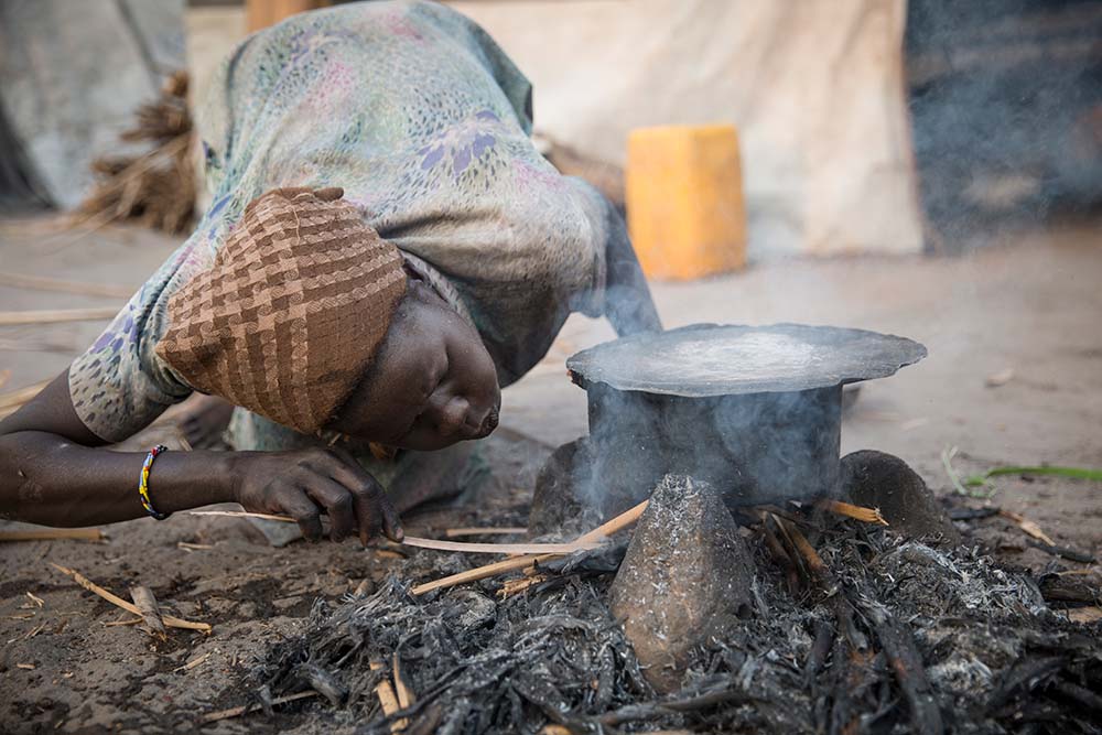 A woman blows on a cooking fire in South Sudan