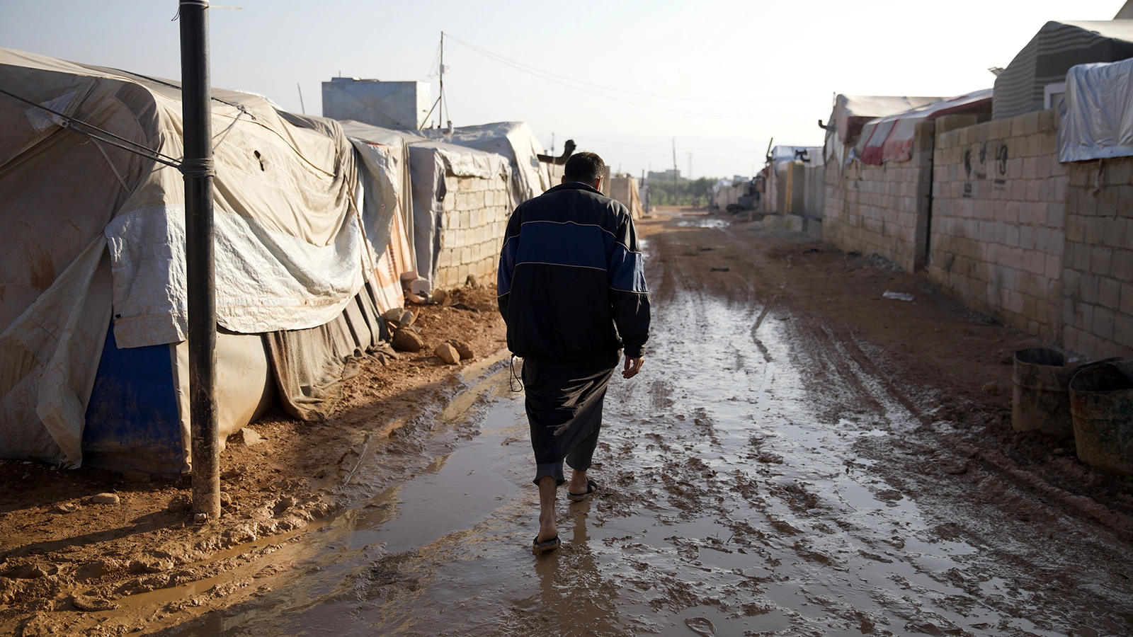 Jaafar* (32) walks through the muddy roads of Ahl al-Khair camp “The condition here is very harsh and staying in a camp is difficult, we did not have any happy occasions in the camp nor any joyful occasion. Do not think that whoever stays here will be happy &quot;This is not true. Anyone who lives here is forced to do so.&quot; Photo: Ali Haj Suleiman/DEC/Fairpicture