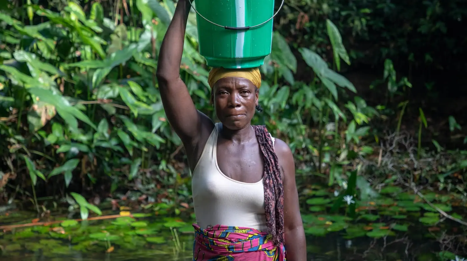 Woman standing in the water with a bucket on her head.