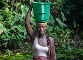 Woman standing in the water with a bucket on her head.