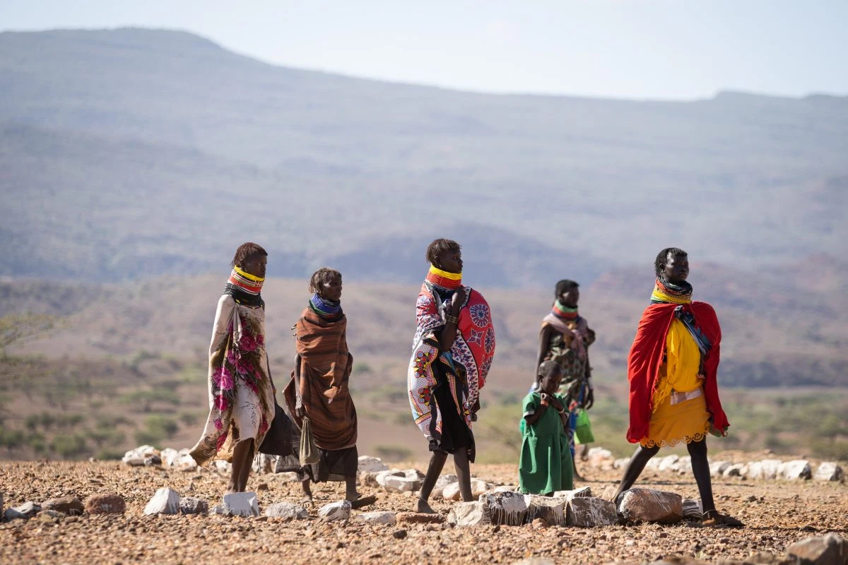 Women and children walk across an arid landscape.