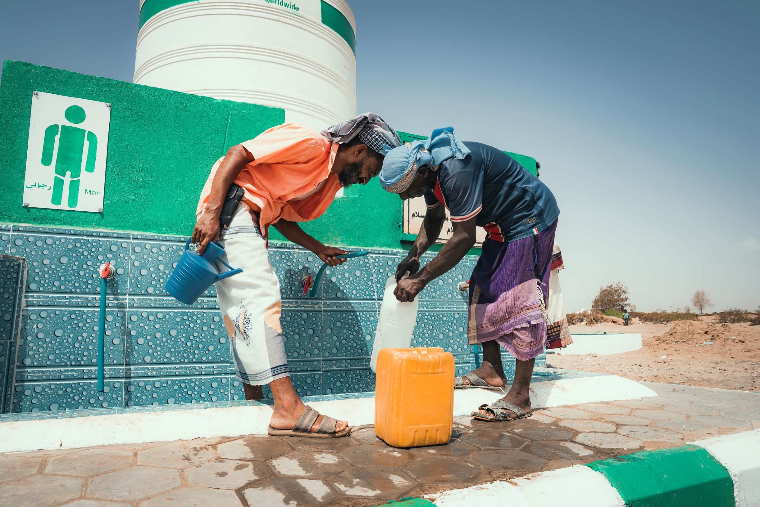 Two men collect water from a water point in Yemen