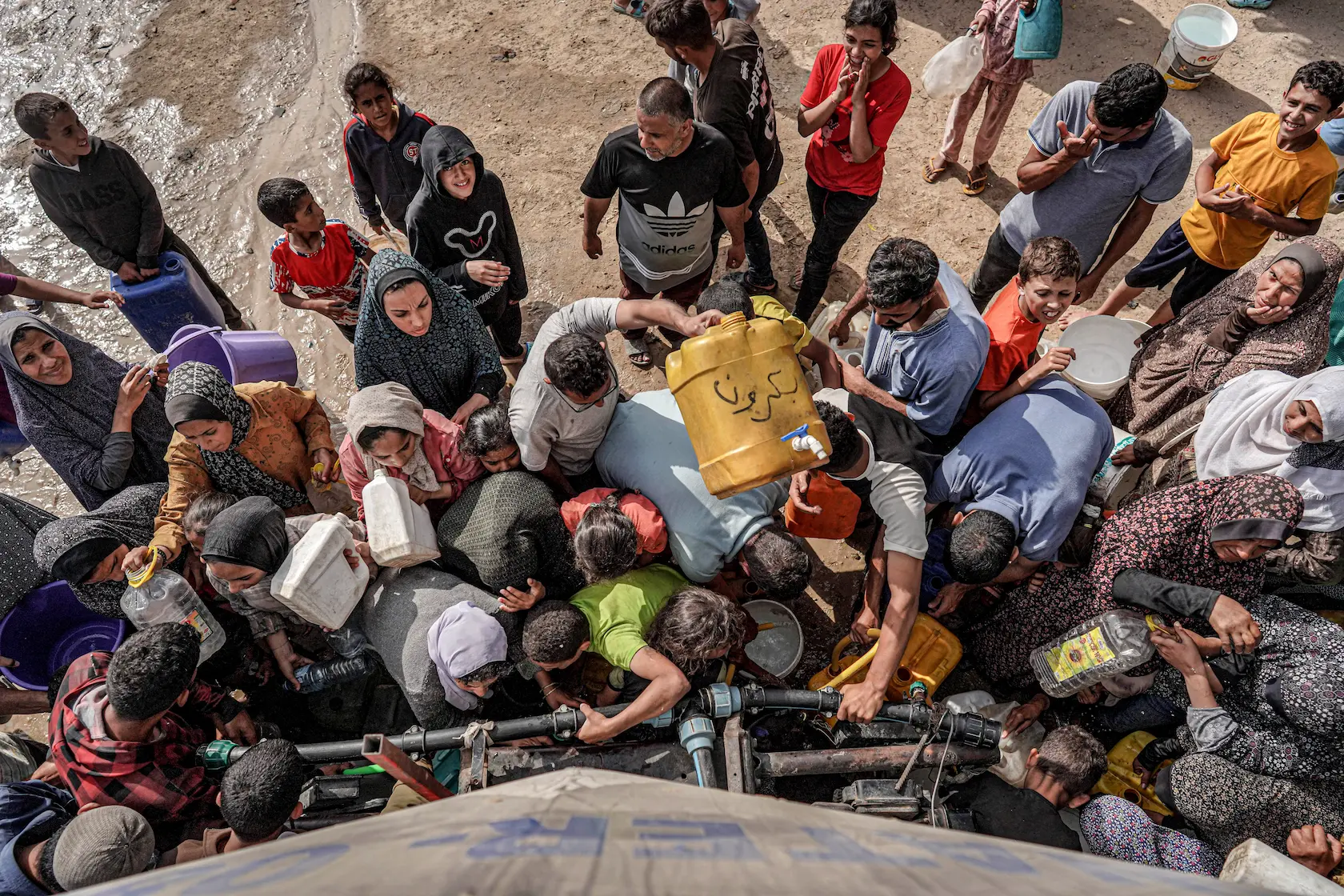 People gather with jerrycans and other containers to collect water from a tanker cistern.